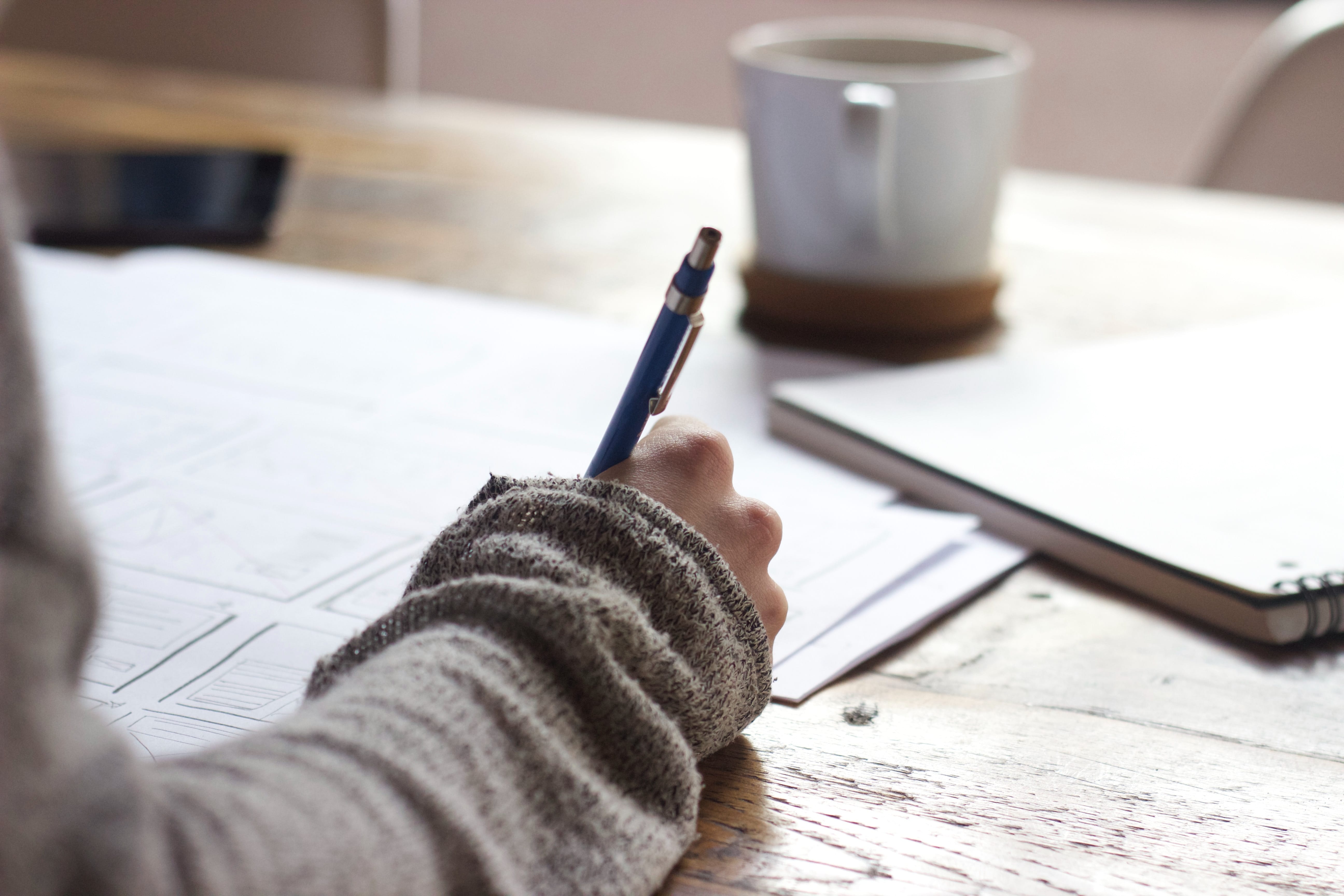 Image of woman at wooden desk, writing with a pen on paper.