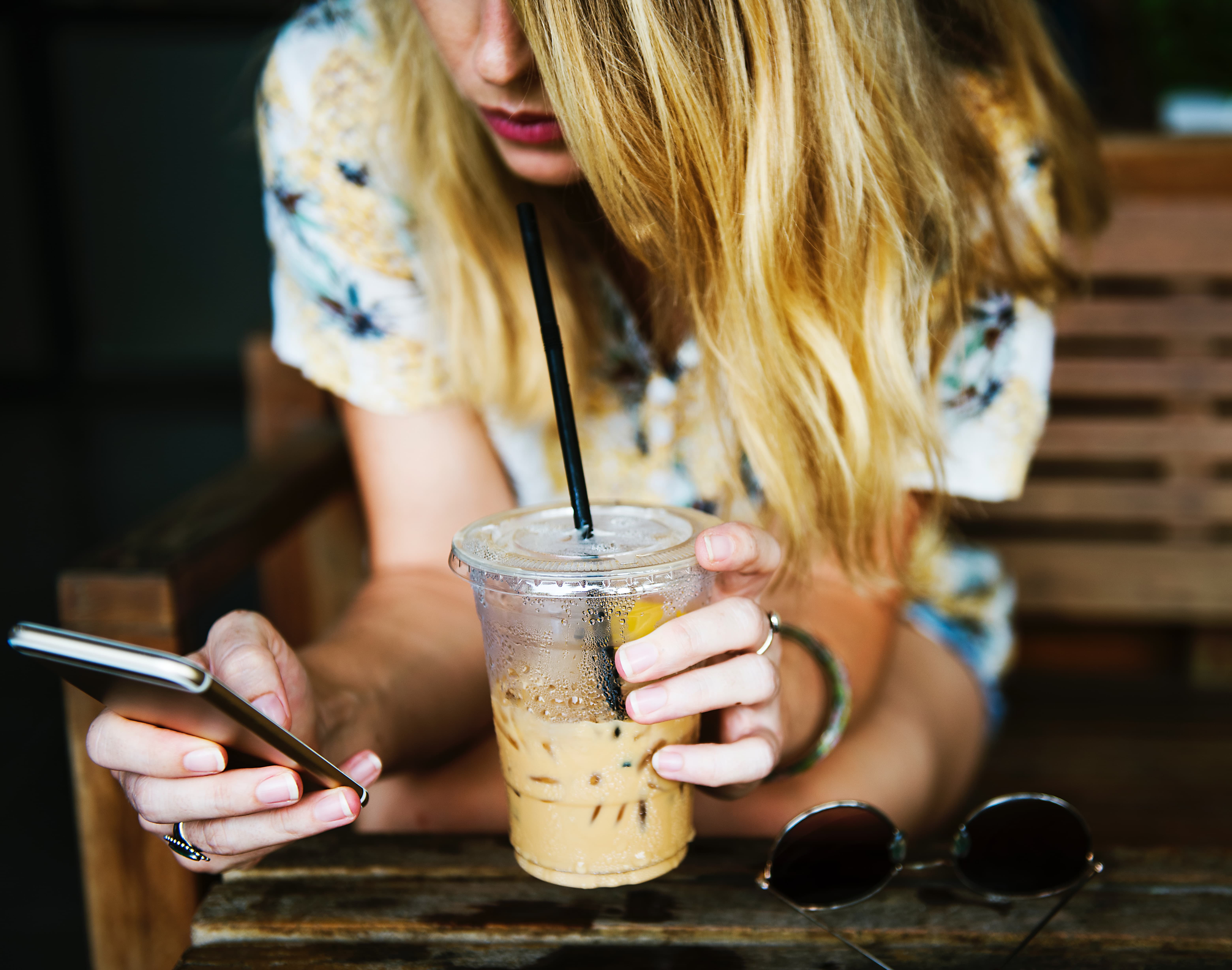 Image of woman on cell phone, drinking iced coffee.