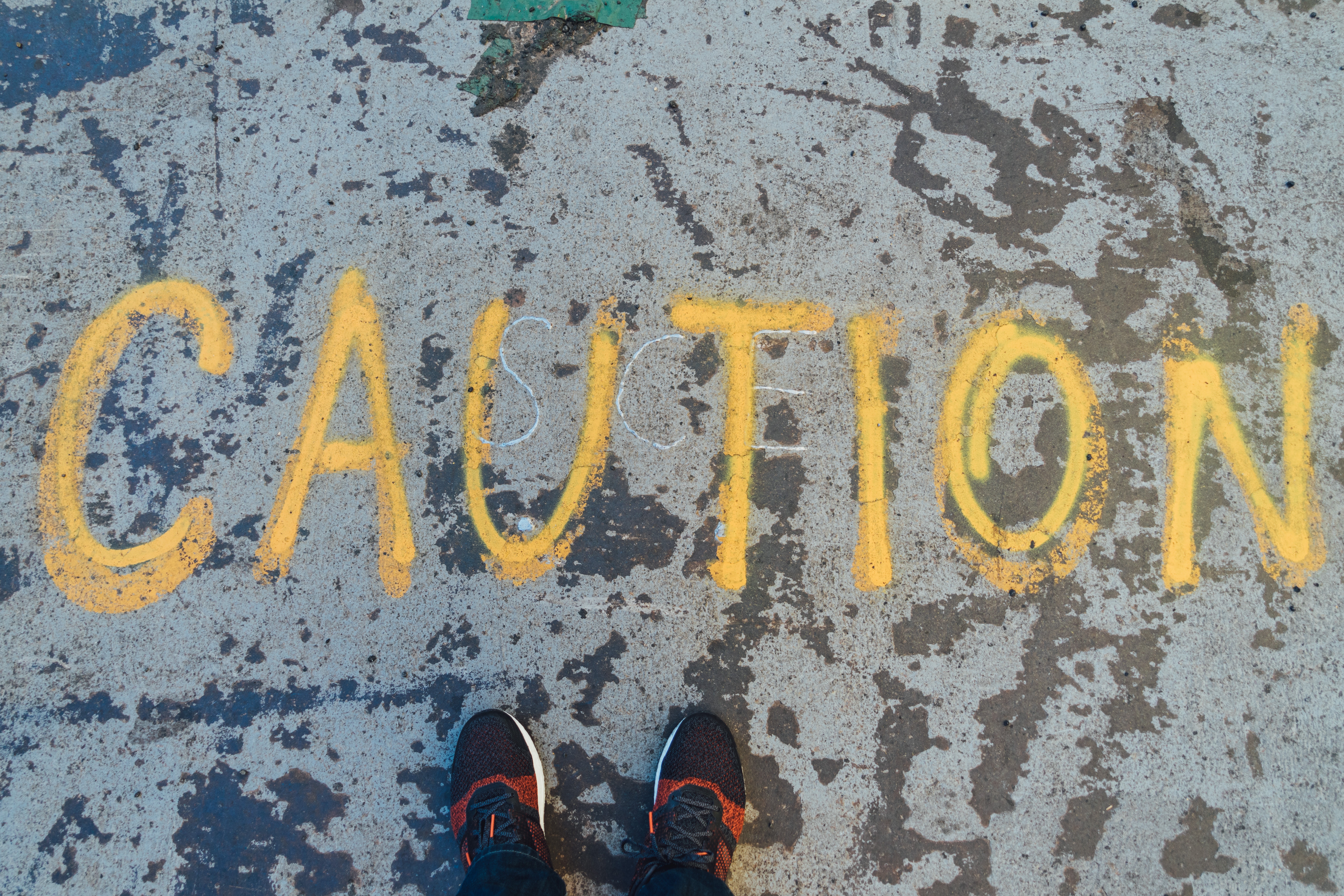 Image of feet standing on top of the word "caution" spray painted on the street