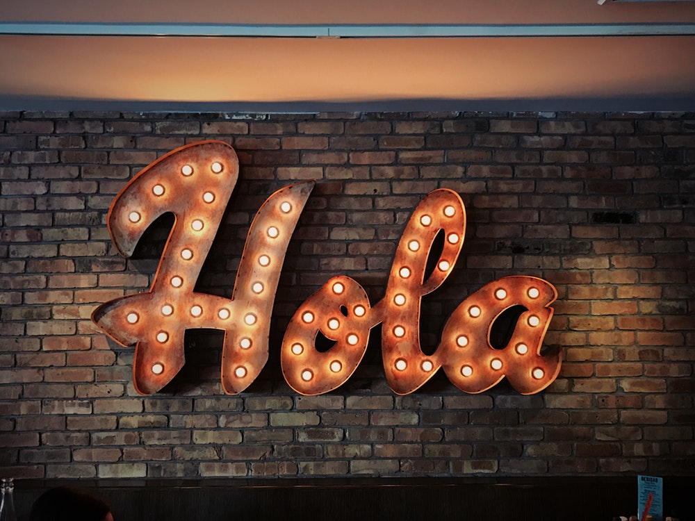 Photo of lit "hola" sign on brown brick wall